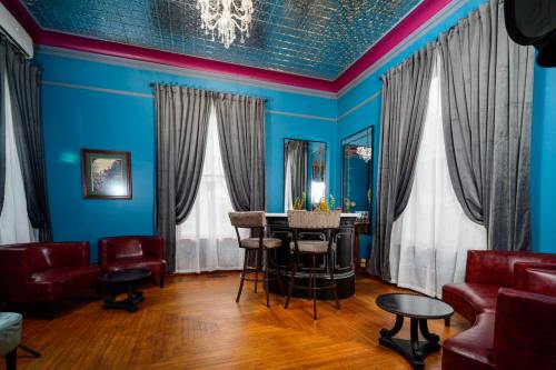A stylish room with blue walls, a chandelier, gray curtains, and a bar area with seating and wooden flooring.