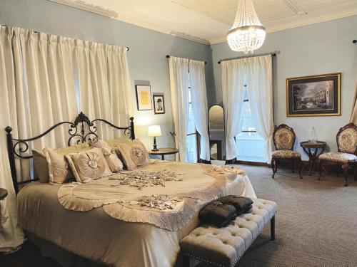 Cozy bedroom with a large bed, elegant decor, chandelier, and two chairs by the window. Soft blue walls and curtains.