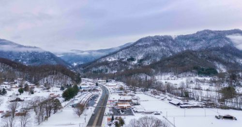 A snowy landscape with mountains in the background, a winding road, and small buildings nestled in the valley.