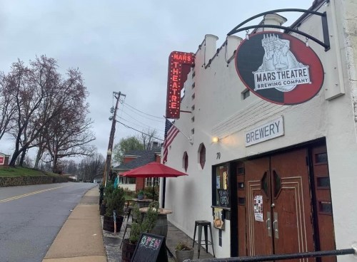 Exterior of Mars Theatre Brewing Company, featuring a sign, outdoor seating, and a cloudy sky.