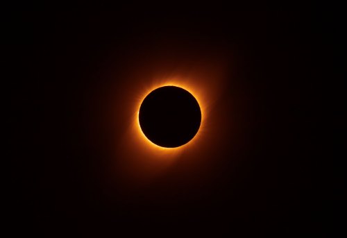 A solar eclipse with a glowing corona surrounding the dark silhouette of the moon against a black sky.