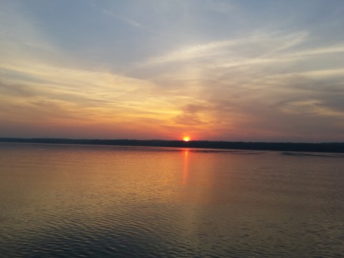 A serene sunset over a calm body of water, with vibrant orange and yellow hues reflecting on the surface.