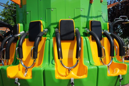 Colorful amusement park ride seats in green and yellow, featuring safety harnesses and a vibrant design.