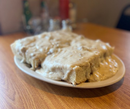 A plate of fluffy biscuits smothered in creamy sausage gravy, served on a wooden table.