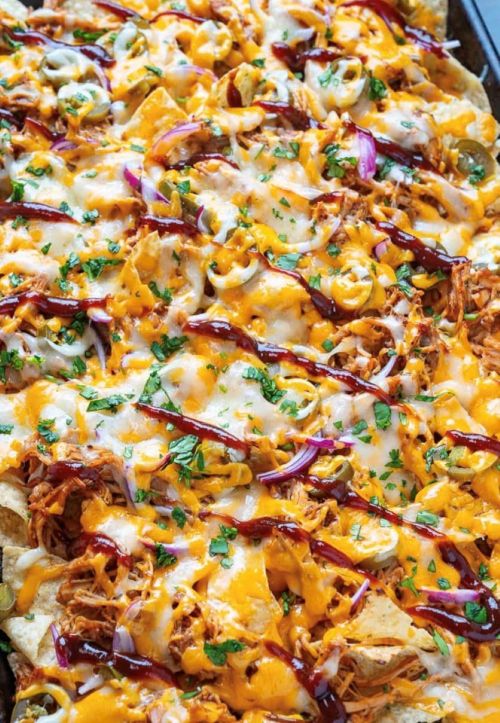 A close-up of loaded nachos topped with shredded chicken, cheese, jalapeños, red onions, and drizzled with sauce.