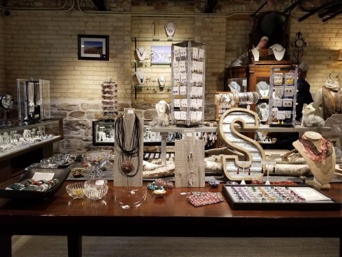 A display of various jewelry pieces and accessories on a wooden table in a well-lit shop.