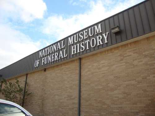 Sign on a building reading "National Museum of Funeral History" against a cloudy sky.