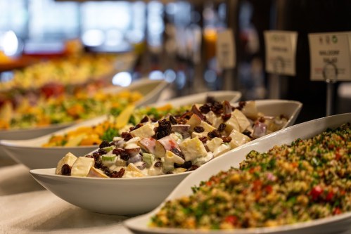 A variety of colorful salads in white bowls, featuring fruits, vegetables, and garnishes on a buffet table.