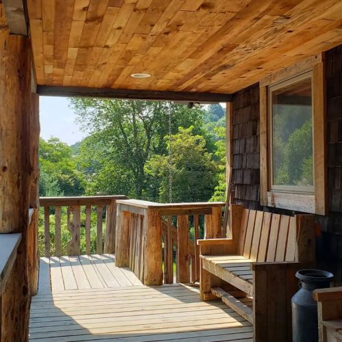 A wooden porch with benches overlooks a lush green landscape and trees under a clear blue sky.