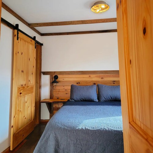 Cozy bedroom with wooden walls, a double bed, and a sliding barn door, illuminated by a warm ceiling light.