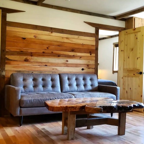 A cozy living room featuring a gray sofa and a unique wooden coffee table against a rustic wood-paneled wall.