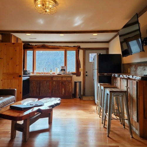 Cozy kitchen with wooden cabinets, a large window, and a rustic dining table. Bright and inviting atmosphere.