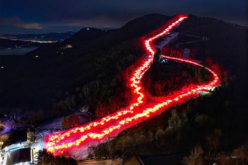 Aerial view of a snowy mountain slope illuminated by red lights, creating a winding path at night.