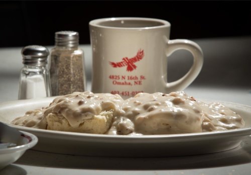 A plate of biscuits smothered in creamy gravy, with a coffee mug and salt and pepper shakers in the background.
