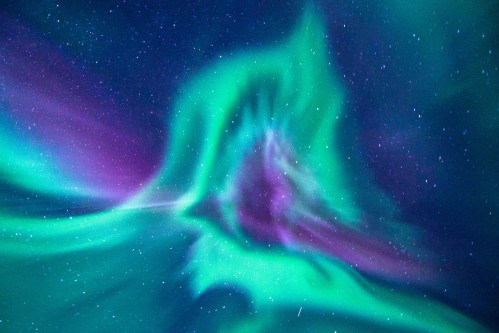 Vibrant aurora borealis with swirling green and purple lights against a starry night sky.
