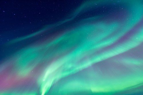 A vibrant display of the northern lights with swirling green and purple hues against a starry night sky.