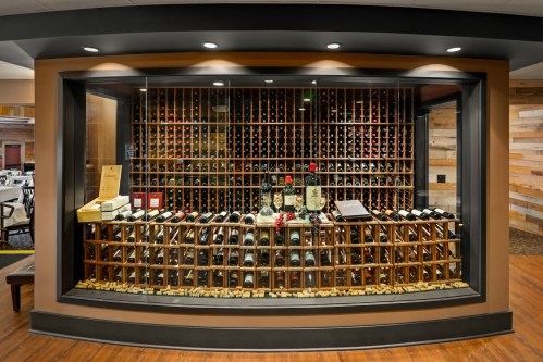 A wine display featuring numerous bottles arranged in a wooden rack, illuminated in a stylish setting.