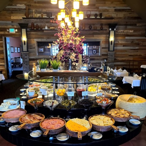 A lavish buffet featuring a variety of cheeses, meats, fruits, and decorative flowers in an elegant restaurant setting.