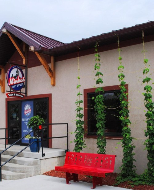 Exterior of Minhas Craft Brewery with a red bench, climbing plants, and a sign for the beer store and museum.