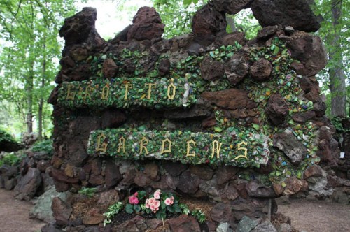 A stone sign covered in greenery reads "Grotto Gardens," surrounded by trees and flowers.