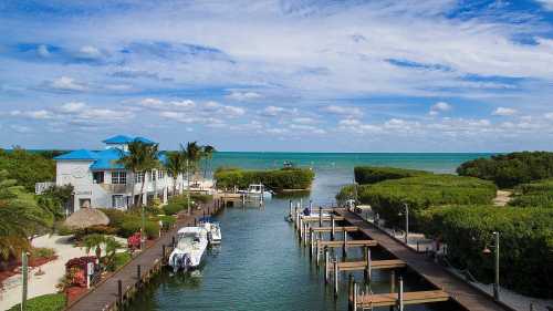 A serene coastal scene featuring a marina with boats, lush greenery, and a blue sky with scattered clouds.