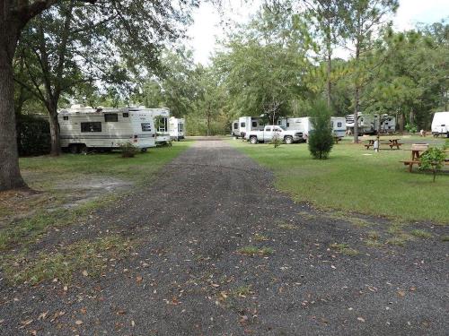 A gravel path leads through a campsite with several RVs and trees in a green, open area.
