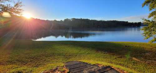 Sunrise over a calm lake, with steps leading down to the water and lush greenery surrounding the scene.