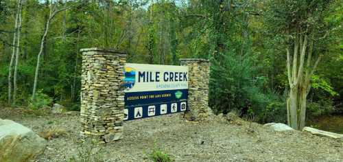 Sign for Mile Creek Park, featuring stone pillars and surrounded by trees, indicating access points for various activities.