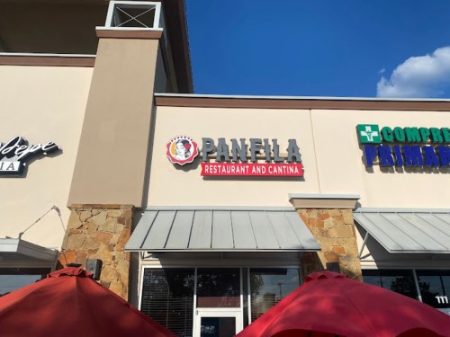 Sign for "Panela Restaurant and Cantina" on a building, with red umbrellas in the foreground.