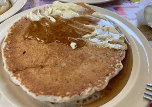 A large pancake topped with butter and syrup on a white plate.