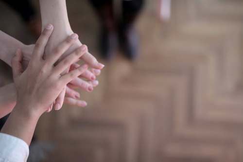 A close-up of several hands stacked together on a wooden floor, symbolizing teamwork and collaboration.