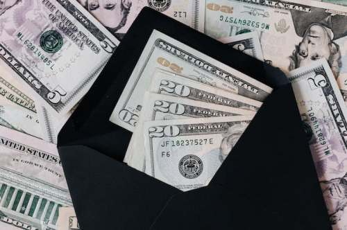 An envelope partially filled with cash, surrounded by various denominations of U.S. dollar bills.