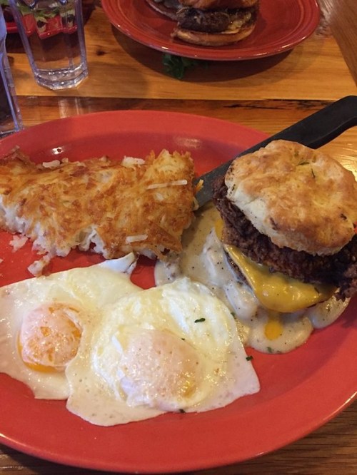 A plate with a biscuit sandwich, hash browns, and two sunny-side-up eggs.