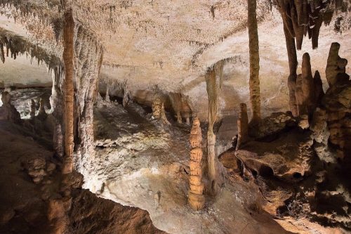 Stalactites and stalagmites in a dimly lit cave, showcasing unique rock formations and textures on the walls and ceiling.
