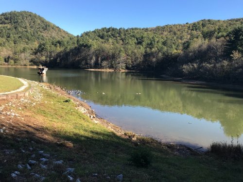 A serene lake surrounded by green hills and trees under a clear blue sky.