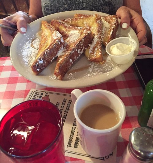 A plate of French toast dusted with powdered sugar, served with a side of whipped cream and a cup of coffee.