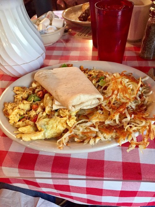 A plate with scrambled eggs, a breakfast burrito, and crispy hash browns on a red and white checkered tablecloth.