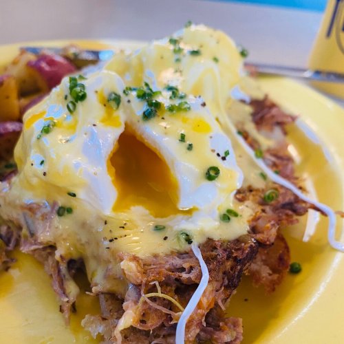 A close-up of a plate featuring pulled pork topped with poached eggs, hollandaise sauce, and green onions.