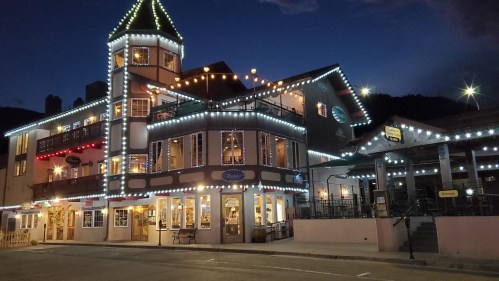 A brightly lit building with festive lights at night, featuring a tower and outdoor seating area.