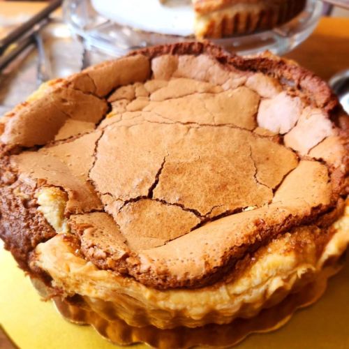 A close-up of a cracked, golden-brown cheesecake with a flaky crust on a golden plate.