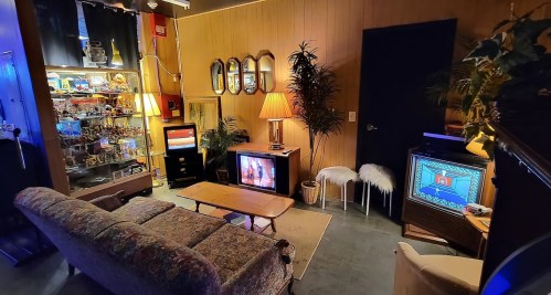 Cozy retro living room with a patterned couch, vintage TVs, lamps, and decorative plants. Warm, inviting atmosphere.