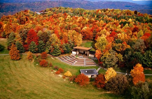 Aerial view of an outdoor amphitheater surrounded by vibrant autumn foliage in a mountainous landscape.