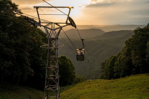 A cable car glides over lush green hills at sunset, with mountains in the background and a serene sky.
