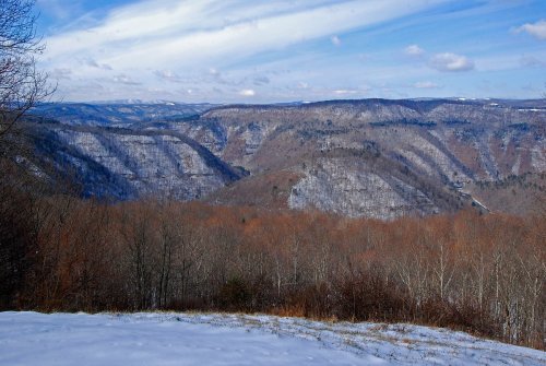 A scenic winter landscape featuring rolling hills, bare trees, and a snowy foreground under a blue sky with clouds.