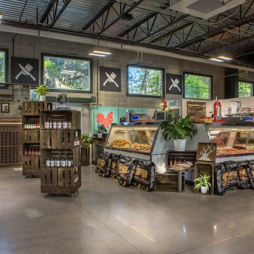 A modern market interior featuring display cases, wooden shelves, and greenery, with large windows and artistic wall decor.