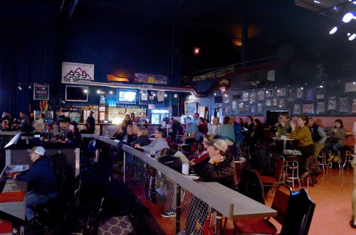 A lively music venue with a crowd seated at tables, a bar area, and walls adorned with framed photos and posters.
