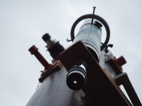 A close-up view of a telescope pointing upwards against a cloudy sky.
