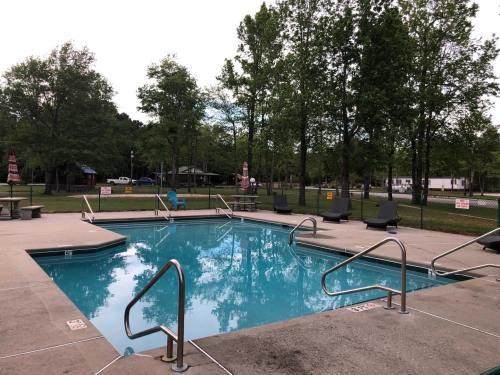A clear swimming pool surrounded by trees and lounge chairs, with a few signs visible in the background.