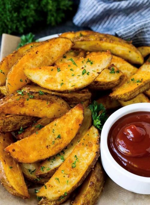 Golden-brown potato wedges garnished with parsley, served with a side of ketchup.