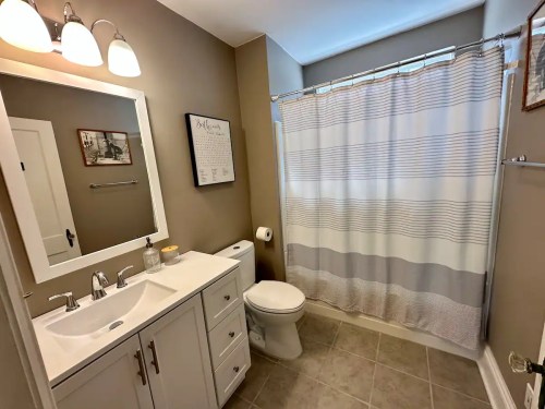 A modern bathroom featuring a white vanity, mirror, shower curtain, and neutral-colored walls and tiles.